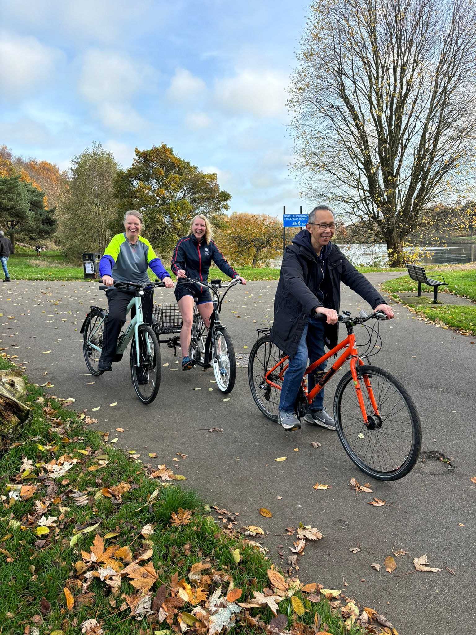 Cyclists on a standard adult bike, electric adult bike and a trike, standing by Witton Lakes.